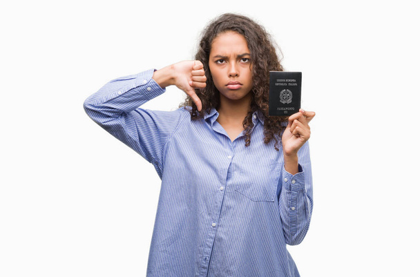 Mujer hispana joven portadora de pasaporte de Italia con la cara enojada, signo negativo que muestra aversión con los pulgares hacia abajo, concepto de rechazo
 - Foto, Imagen