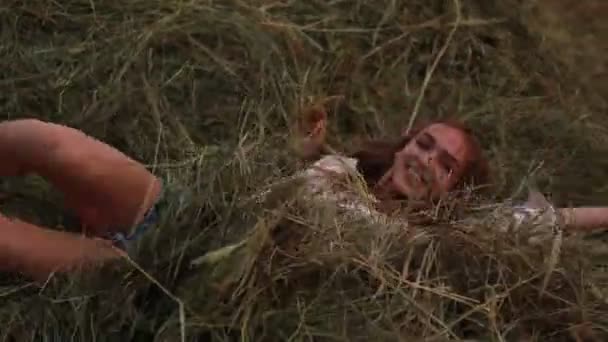 Young woman rolls over at  haystack, throws bunch of hay and she has fun. - Footage, Video