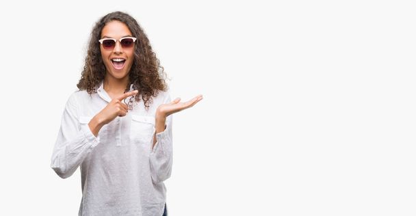 Jonge Spaanse vrouw, dragen van een zonnebril erg blij met de hand en de vinger te wijzen - Foto, afbeelding