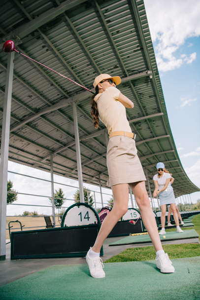 χαμηλή γωνία προβολής των γυναικών με μπαστούνια του γκολφ παίζουν γκολφ στο γήπεδο γκολφ - Φωτογραφία, εικόνα