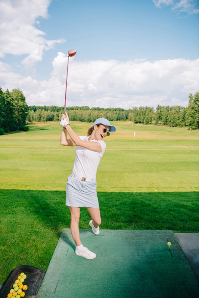 вид сбоку женщины в поло, солнцезащитных очках и кепке, играющей в гольф на поле для гольфа
 - Фото, изображение