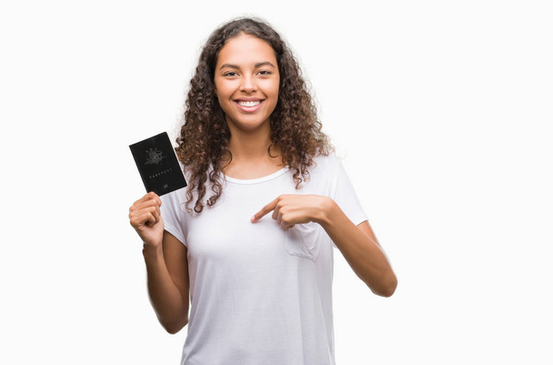Young hispanic woman holding passport of Australia with surprise face pointing finger to himself - Фото, изображение