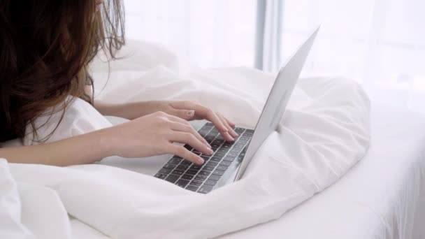 Beautiful Asian woman playing computer or laptop while lying on the bed in her bedroom. Happy female buying online shopping at home. Lifestyle woman at home concept.  - Filmmaterial, Video
