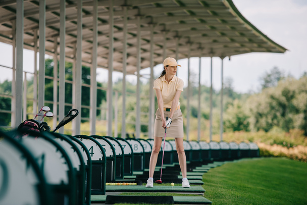 Frau mit gelber Mütze und Polo spielt Golf auf Golfplatz - Foto, Bild