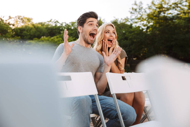 Surprised screaming lovely young couple sitting together on chairs and watching film outdoors - Photo, image