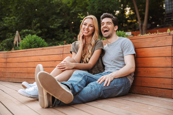 Cheerful lovely young couple having fun and looking away while sitting together outdoors - Foto, imagen