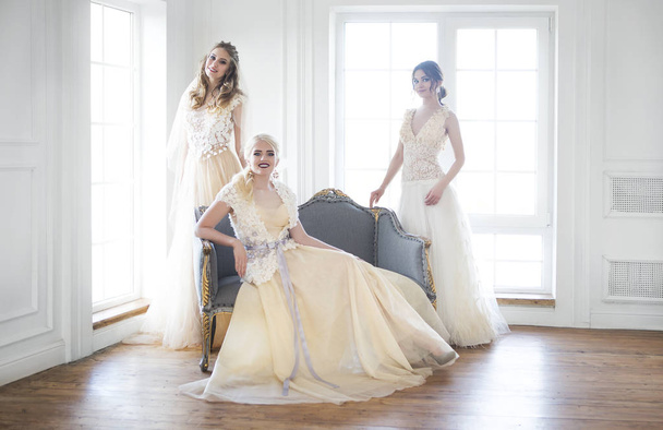 Tres mujeres jóvenes cerca de la ventana con vestidos de novia
 - Foto, imagen