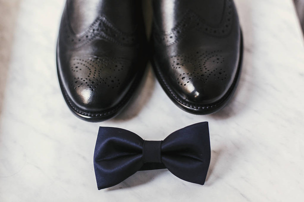 stylish black shoes and navy bow tie on marble background, top view. groom morning wedding preparations - Photo, image