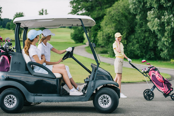 вид збоку жіночого гольфу в кепках у візку для гольфу і друг розмовляє на смартфоні на полі для гольфу
 - Фото, зображення