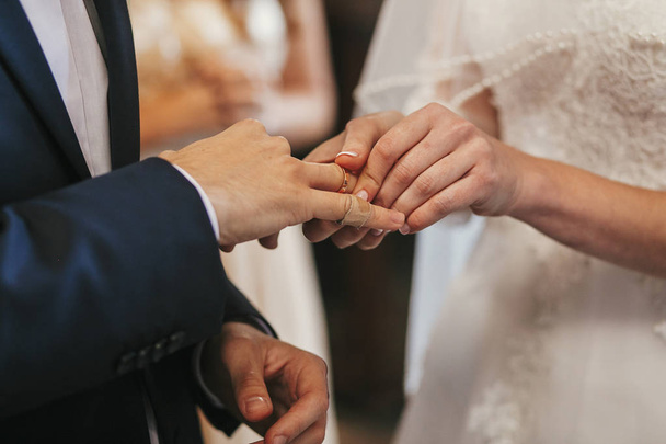 schöne Brautpaare, die während der Trauung Trauringe in der Kirche austauschen. spirituelle heilige Ehe. Hochzeitspaar und Priester ziehen Ringe an - Foto, Bild