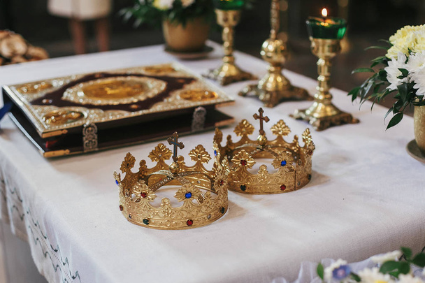 黄金の冠と教会での結婚式の間に神聖な祭壇の上の聖書。神聖な結婚の精神的な瞬間 - 写真・画像