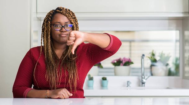 Afrikaanse Amerikaanse vrouw om thuis te zitten met boos gezicht, minteken weergegeven: afkeer met duimen naar beneden, afwijzing concept - Foto, afbeelding