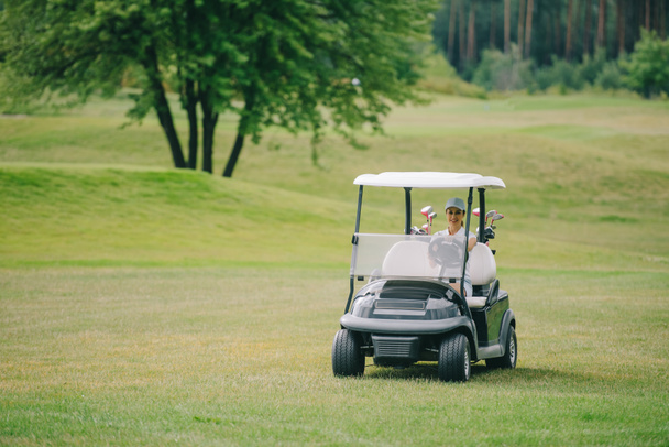 woman in cap riding golf cart at golf course on summer day - Photo, Image