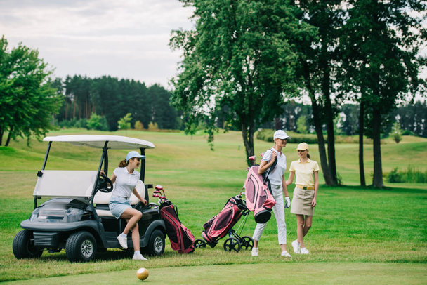group of female golf players in caps with golf equipment at golf course on summer day - Fotografie, Obrázek