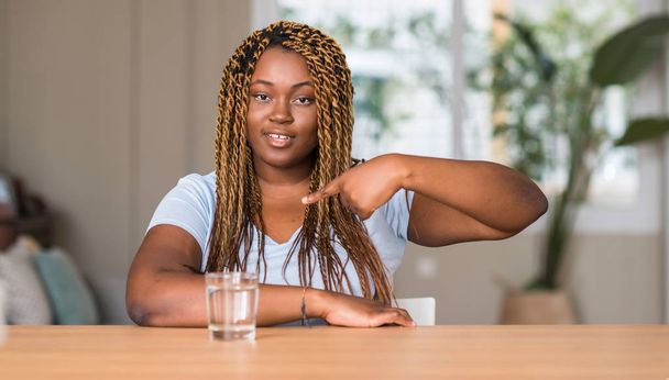 Afrikanische Amerikanerin trinkt Wasser mit überraschendem Gesicht und zeigt mit dem Finger auf sich selbst - Foto, Bild