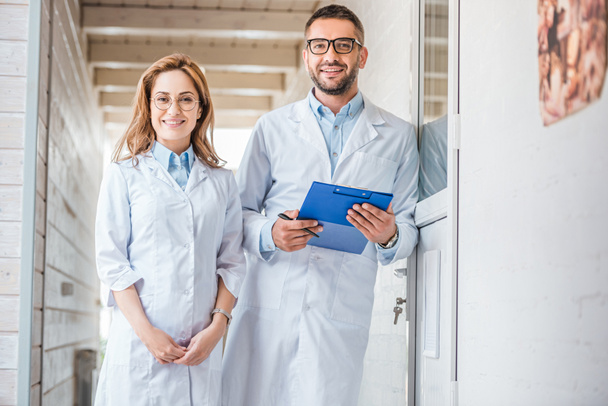 two veterinarians in white coats standing in veterinary clinic and looking at camera - Fotoğraf, Görsel