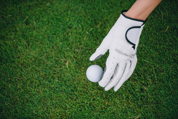 vista parcial de la mujer en el guante de golf poniendo pelota en el césped verde en el campo de golf
 - Foto, Imagen