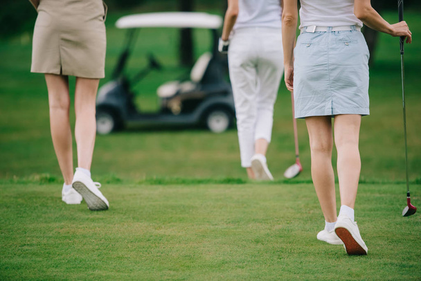 tiro recortado de mulheres com tacos de golfe andando no gramado verde no campo de golfe
 - Foto, Imagem
