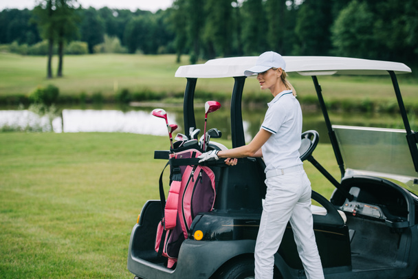 femme en polo et casquette avec équipement de golf debout à la voiturette de golf sur le terrain de golf le jour d'été
 - Photo, image