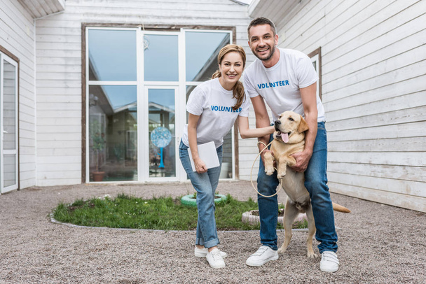 smiling volunteers of animals shelter palming labrador and looking at camera - Fotografie, Obrázek