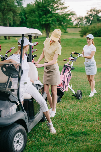 female golf players in caps at golf cart on golf course - Foto, Imagem