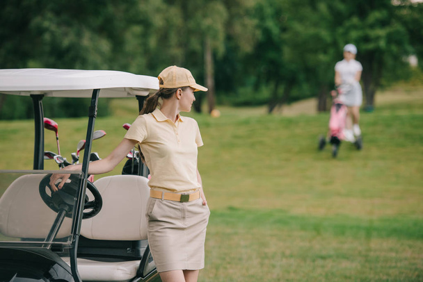 selective focus of female golf player in cap at golf cart on green lawn - Φωτογραφία, εικόνα
