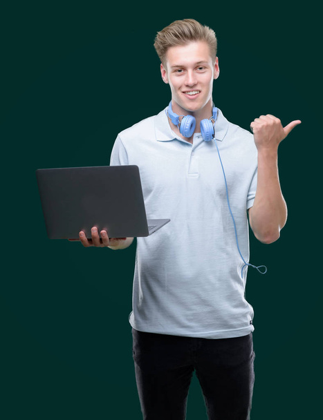 Young handsome blond man using a laptop pointing with hand and finger up with happy face smiling - Photo, image
