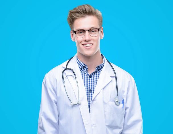 junge hübsche blonde Ärztin mit einem glücklichen Gesicht stehend und lächelnd mit einem selbstbewussten Lächeln, das Zähne zeigt - Foto, Bild