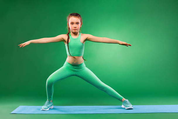 Kid girl doing fitness exercises on green background - Foto, Imagen