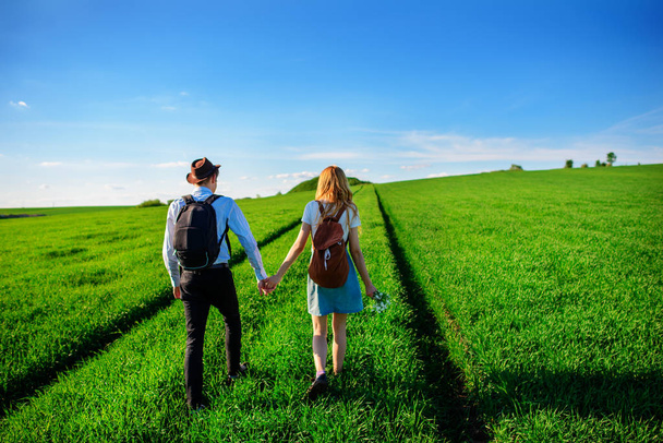 Z plecakiem mężczyzna w kapeluszu i kobieta z długimi włosami iść wzdłuż ścieżki. Kilka spacerów wzdłuż łąki. - Zdjęcie, obraz
