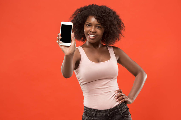 Portrait of a confident casual afro girl showing blank screen mobile phone isolated over red background - Foto, Bild