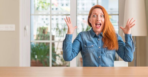 Femme rousse à la maison célébrant fou et étonné pour le succès avec les bras levés et les yeux ouverts hurlant excités. Concept gagnant
 - Photo, image