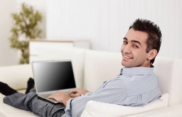 Przystojny mężczyzna jest używany komputer przenośny, patrząc na kamery i uśmiechając się - Zdjęcie, obraz
