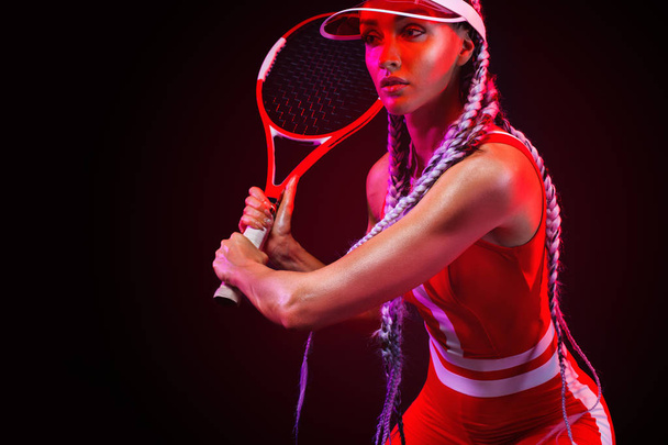 Tennis player. Beautiful woman athlete with racket in red costume and hat isolated on black background. Fashion and sport concept. - Valokuva, kuva