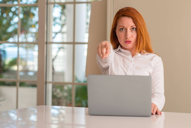 Руда жінка використовує комп'ютерний ноутбук вдома, вказуючи пальцем на камеру і до вас, знак руки, позитивний і впевнений жест спереду
 - Фото, зображення