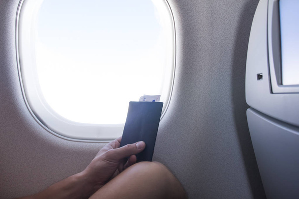 Man with passport and ticket sitting next to window in aircraft cabin airplane vacation journey. Traveling by plane. - Zdjęcie, obraz