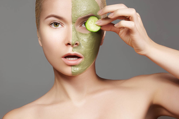Beautiful Woman Applying Green Facial Mask. Beauty Treatments. Close-up Portrait of Spa Girl Apply Clay Facial mask and Cucumber on grey background - 写真・画像