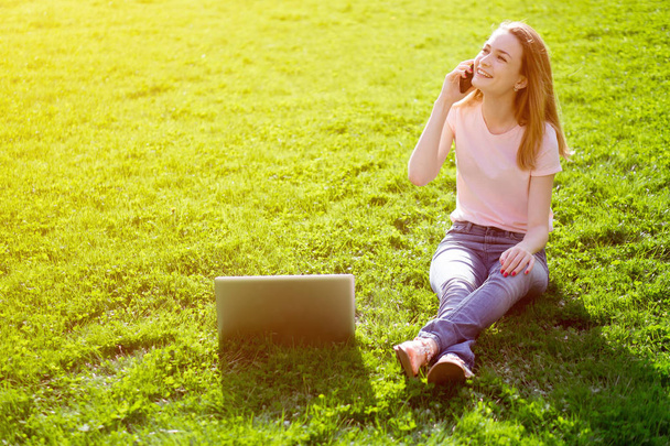 girl on the lawn with a laptop and talking on the phone - Foto, Bild