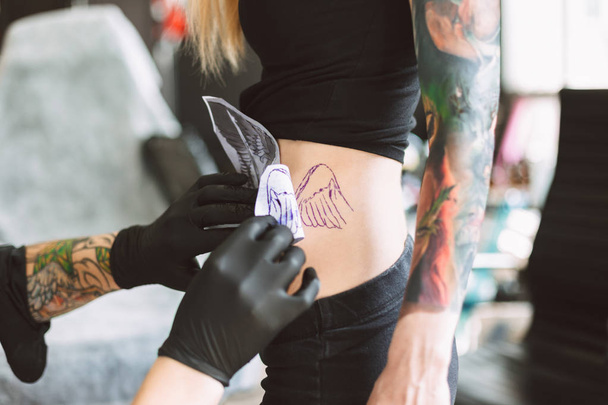 Close up tattooer in black gloves preparing new tattoo on girl body in modern tattoo studio - Photo, Image