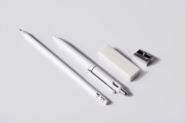 Nahaufnahme von Stift mit Bleistift, Radiergummi und Spitzer in Reihe auf weißer Oberfläche für Attrappe - Foto, Bild