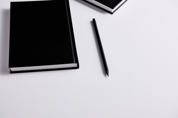 close-up shot of black hard cover notebooks with pencil on white surface - Valokuva, kuva