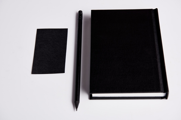 primer plano de cuaderno negro con lápiz y tarjeta de visita en blanco en la superficie blanca para maqueta
 - Foto, Imagen