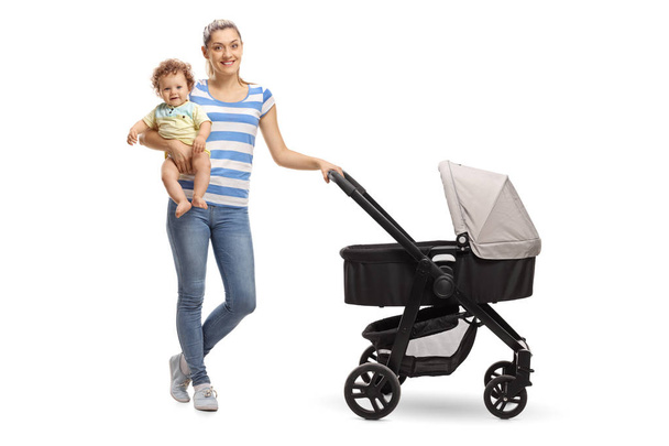 Full length portrait of a young mother with her baby and a stroller isolated on white background - Valokuva, kuva