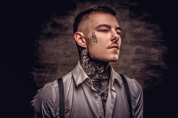 Retrato de cerca de un joven tatuado a la antigua con camisa blanca y tirantes. Aislado sobre un fondo oscuro
. - Foto, imagen
