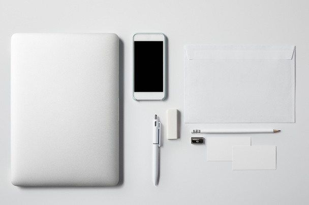 top view of laptop with smartphone and office supplies on white tabletop for mockup - Foto, Bild
