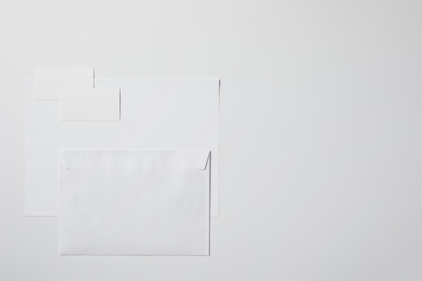 pohled shora prázdného papíru, obálek a vizitek na bílém povrchu pro makety - Fotografie, Obrázek
