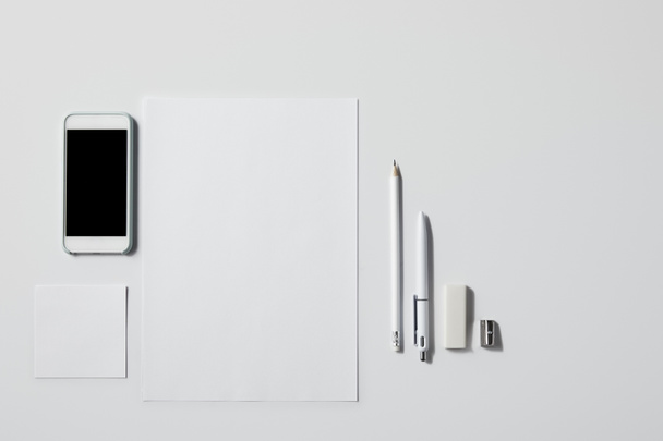 вид сверху на смартфон с различными принадлежностями на белом столе для макета
 - Фото, изображение