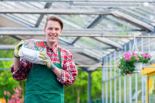 Cheerful young man carrying a bag of potting soil while working  - Photo, Image