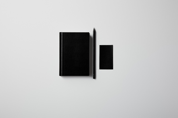 κάτοψη του μαύρο σημειωματάριο με μολύβι και κενό επαγγελματική κάρτα σε λευκή επιφάνεια για mockup - Φωτογραφία, εικόνα