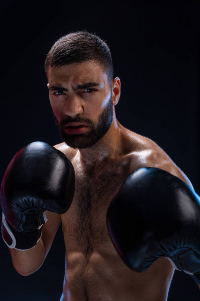 Portrait of tough male boxer posing in boxing stance against black background. - Фото, изображение